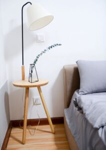 Modern minimalist bedroom with wooden nightstand, sleek lamp, and gray bedding set.